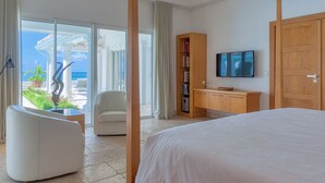 Una camera d'hotel moderna con un grande letto, una televisione, un armadio in legno e vista sull'oceano attraverso un'ampia porta scorrevole in vetro.