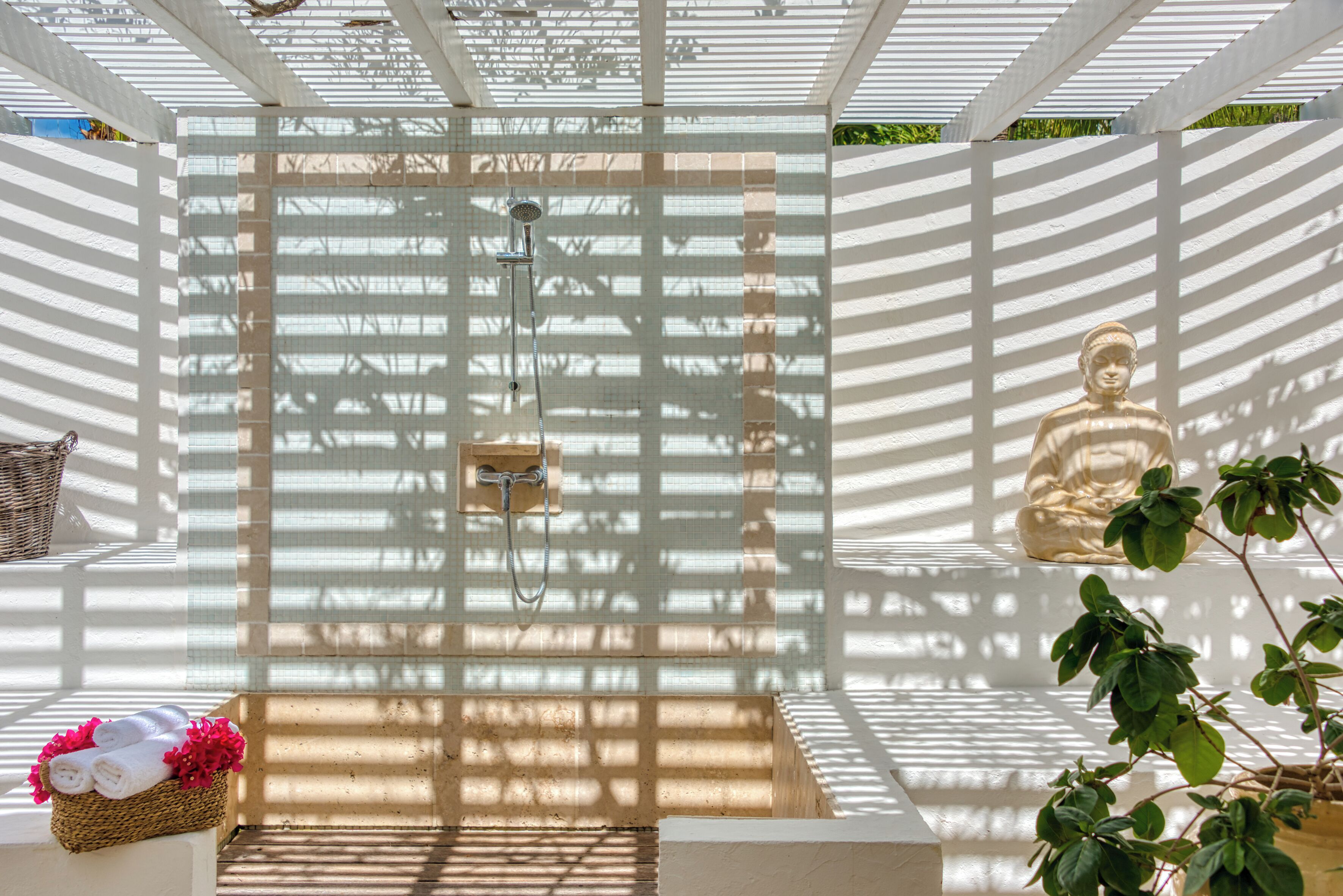 A spa area with a shower, a meditation statue, and a basket of towels.