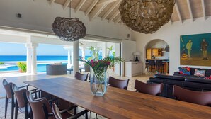 Un'ampia sala da pranzo con un tavolo e sedie in legno, un vaso con fiori e vista sull'oceano.
