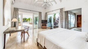 A spacious bedroom with a large bed, a desk with a chair, a television, and a balcony with curtains. - Villa Bamboo | Ocean View - Located in  Wonderful Terres Basses with Private Pool (Les Terres Basses)