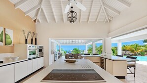 A modern kitchen with an island, built-in oven, and a view of the pool and ocean. - Villa Bamboo | Ocean View - Located in  Wonderful Terres Basses with Private Pool (Les Terres Basses)