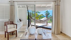 A modern room with a view of palm trees and the ocean, a hammock, a wooden chair, and two white spherical objects on a wooden table.