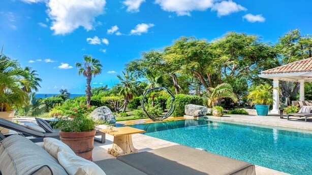 A poolside area with lounge chairs, a pergola, and a view of the ocean.