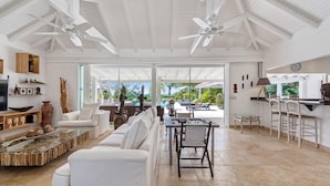 A spacious living area with a white sofa, a dining table with chairs, and a ceiling fan.
