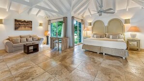 A spacious bedroom with a large bed, a sofa, and a small table. There is a ceiling fan and a window with curtains.