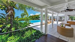 Un espacio al aire libre cubierto con piscina, sillas de descanso y plantas tropicales.