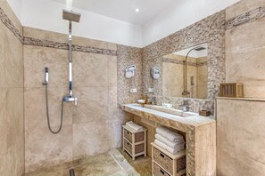 A modern bathroom with a stone wall, a large mirror, a shower, and a vanity with a sink and towel storage.