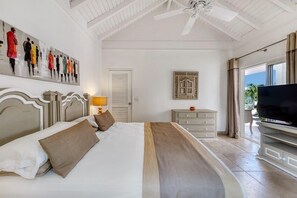 A hotel room with a bed, a television, a ceiling fan, and a painting on the wall.