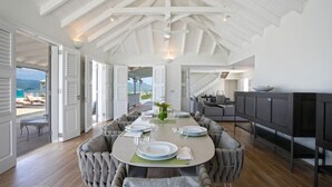 A spacious dining area with a high ceiling and open doors leading to a balcony with a view of the sea. - Villa Le Caprice | Beach Front - Located in  Tropical Baie Rouge with Private Pool (Lowlands)