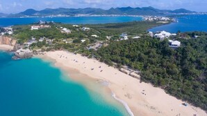 An aerial view of a beach with clear turquoise waters, a sandy shore, and buildings on a hillside. - Villa Le Caprice | Beach Front - Located in  Tropical Baie Rouge with Private Pool (Lowlands)