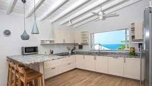 A modern kitchen with a large island, wooden bar stools, and a view of the ocean. - Villa Le Caprice | Beach Front - Located in  Tropical Baie Rouge with Private Pool (Lowlands)