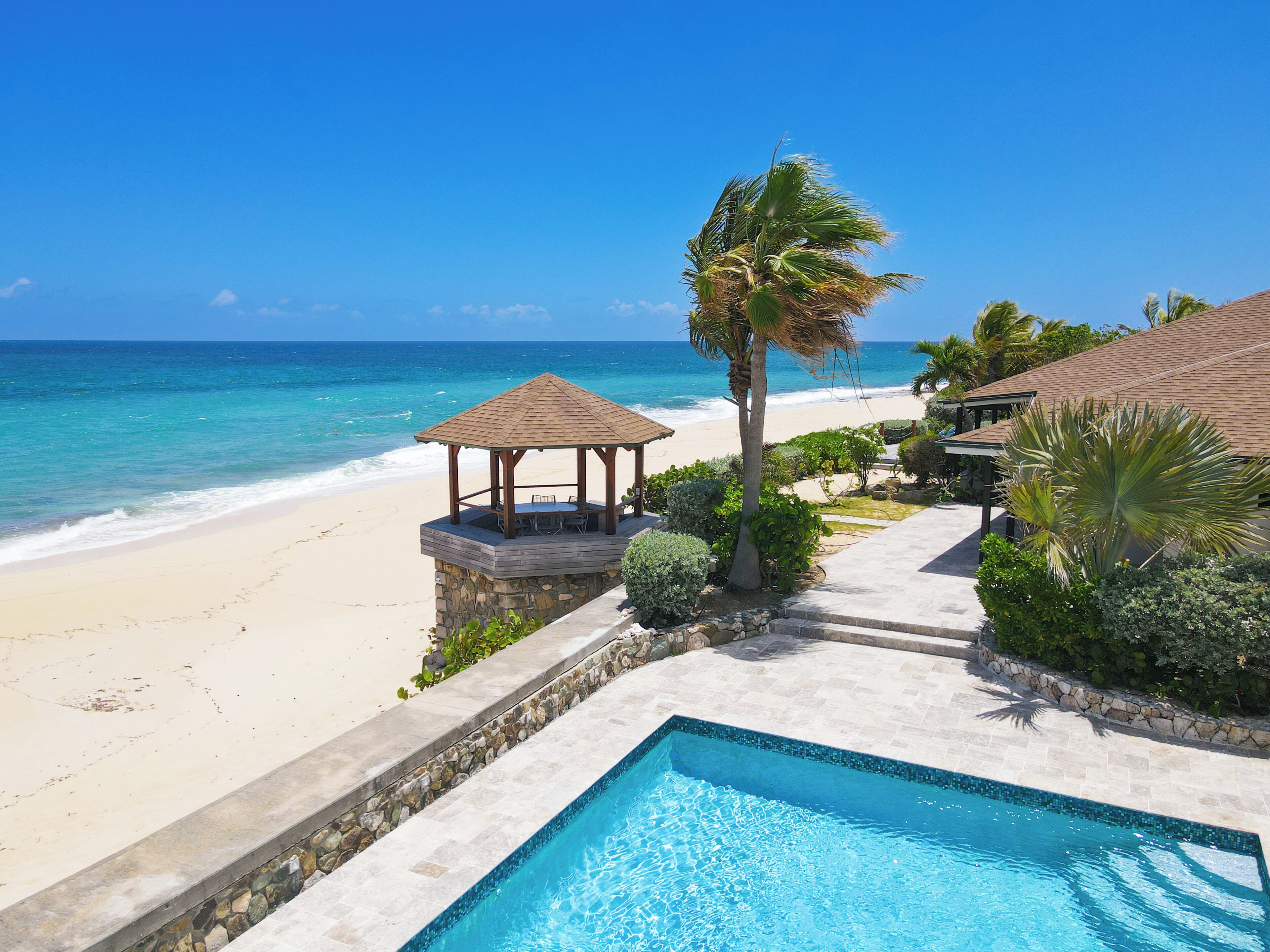A beachside pool with a gazebo, palm trees, and a view of the ocean.
