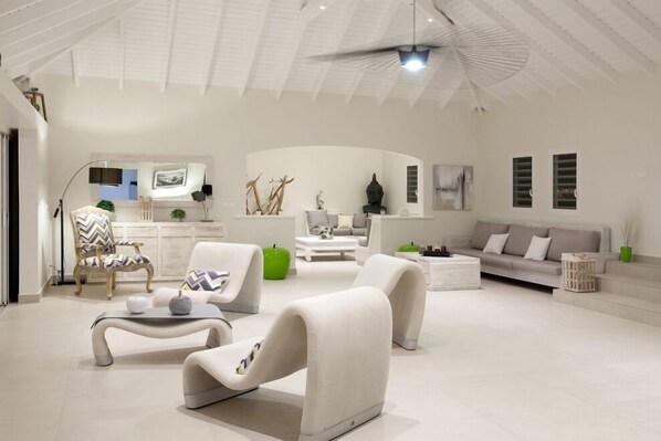 Un salon moderne avec un plafond haut, des meubles blancs et un ventilateur de plafond.