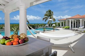 Un espace aménagé au bord de la piscine, avec une table garnie de fruits, un hamac et des chaises longues.