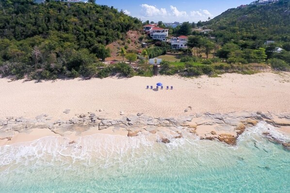 Una playa con agua turquesa cristalina, costa rocosa y una hilera de sillas azules.