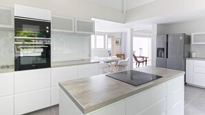 Et moderne køkken med hvide skabe, indbygget ovn, køleskab og et spiseområde med bord og stole.