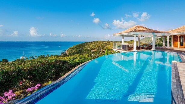 A pool with a clear view of the ocean, a covered seating area, and a building with a tiled roof. - Villa Happy Bay  | Beach View - Located in  Beautiful Happy Bay with Private Pool (Saint Martin)
