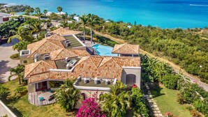 A large villa with multiple roofs and a swimming pool, surrounded by lush greenery and a view of the sea. - Villa Happy Bay  | Beach View - Located in  Beautiful Happy Bay with Private Pool (Saint Martin)