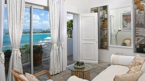 A balcony with a view of the sea, a white sofa, wicker chairs, and a round table with a plant.