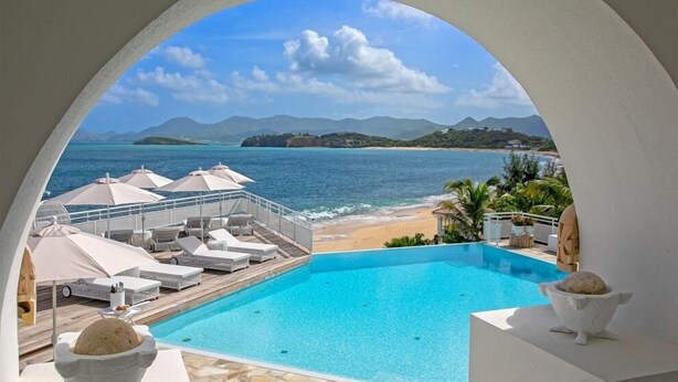 A pool area with lounge chairs and umbrellas, overlooking a beach and the sea.