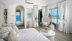 A bedroom with a bed, a chair, a round table, and a view of the ocean.