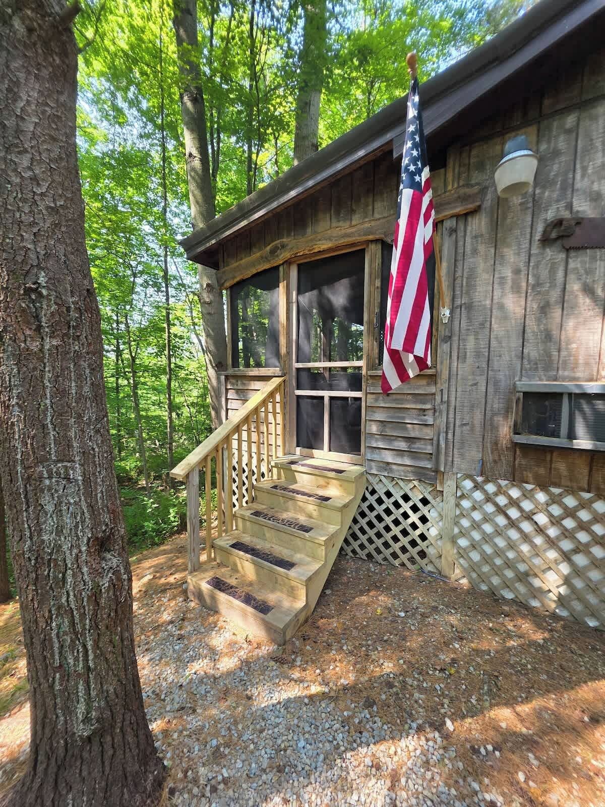 Eine Holzhütte mit Veranda, Treppe und einer amerikanischen Flagge.
