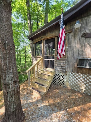 A wooden cabin with a porch, a staircase, and an American flag.