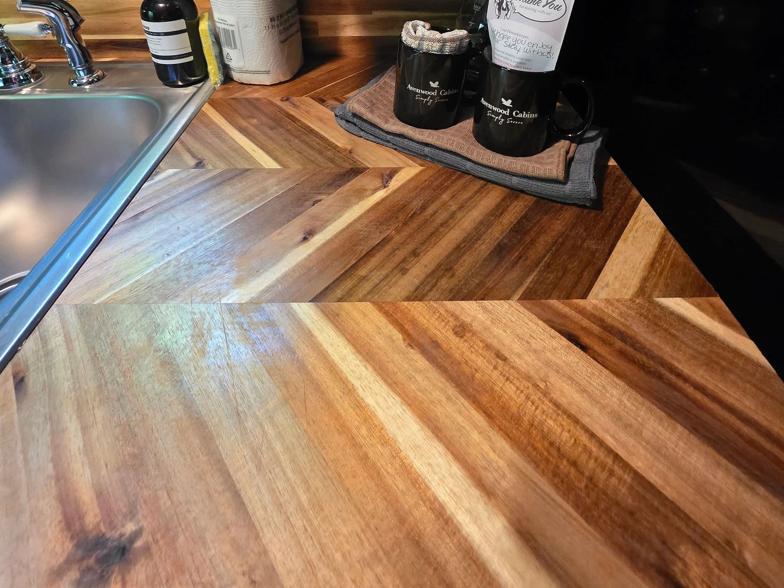A kitchen counter with a modern design, featuring a stainless steel sink and wooden flooring.