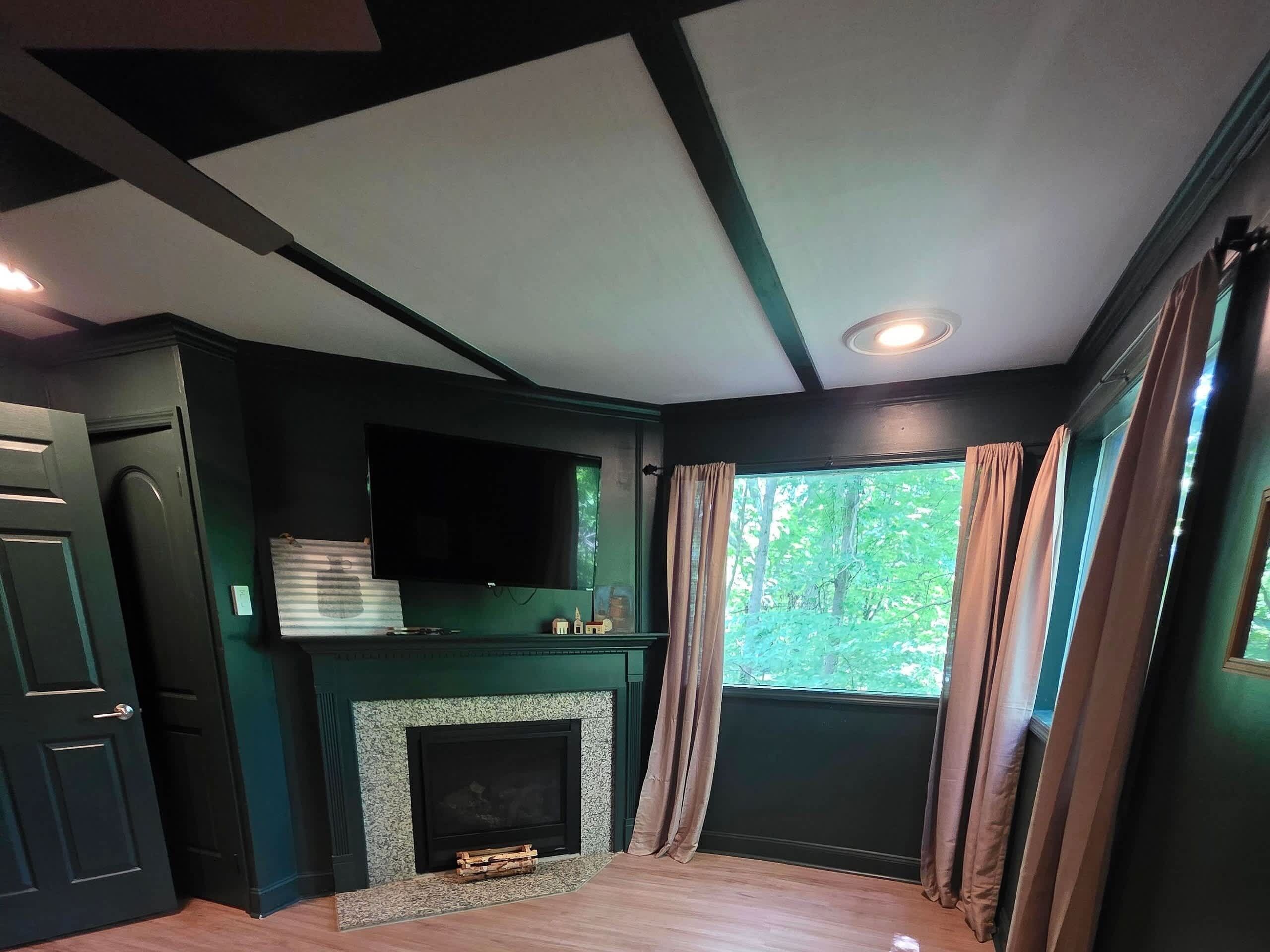 A room with a fireplace, a television mounted above it, and a window with curtains.