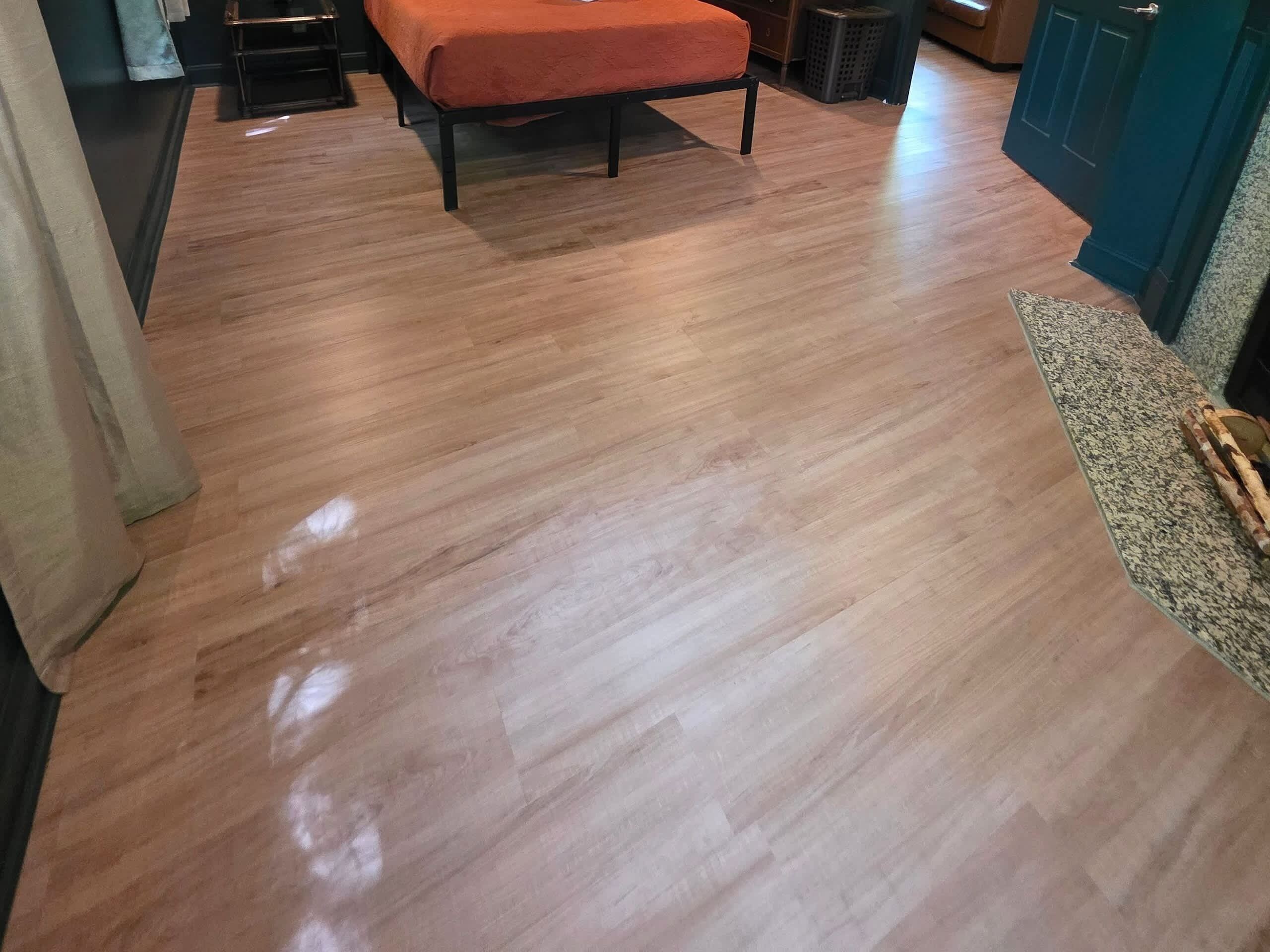 Ein Zimmer mit Holzboden, einem Bett mit orangefarbener Decke und einer Tür zu einem weiteren Raum.
