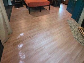 Une pièce avec un plancher en bois, un lit recouvert d’une couverture orange et une porte qui donne sur une autre pièce.
