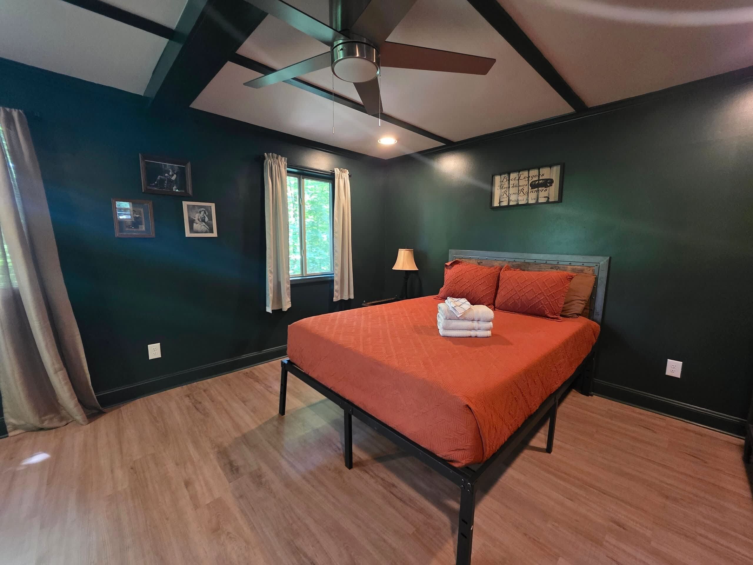 Une chambre à coucher comprenant un lit, un ventilateur de plafond, une fenêtre avec des rideaux et des œuvres d’art accrochées au mur.