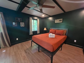 Une chambre à coucher comprenant un lit, un ventilateur de plafond, une fenêtre avec des rideaux et des œuvres d’art accrochées au mur.