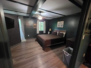 Ein Schlafzimmer mit einem Bett, einem Deckenventilator, einem Fenster mit Vorhängen und einem Mülleimer.