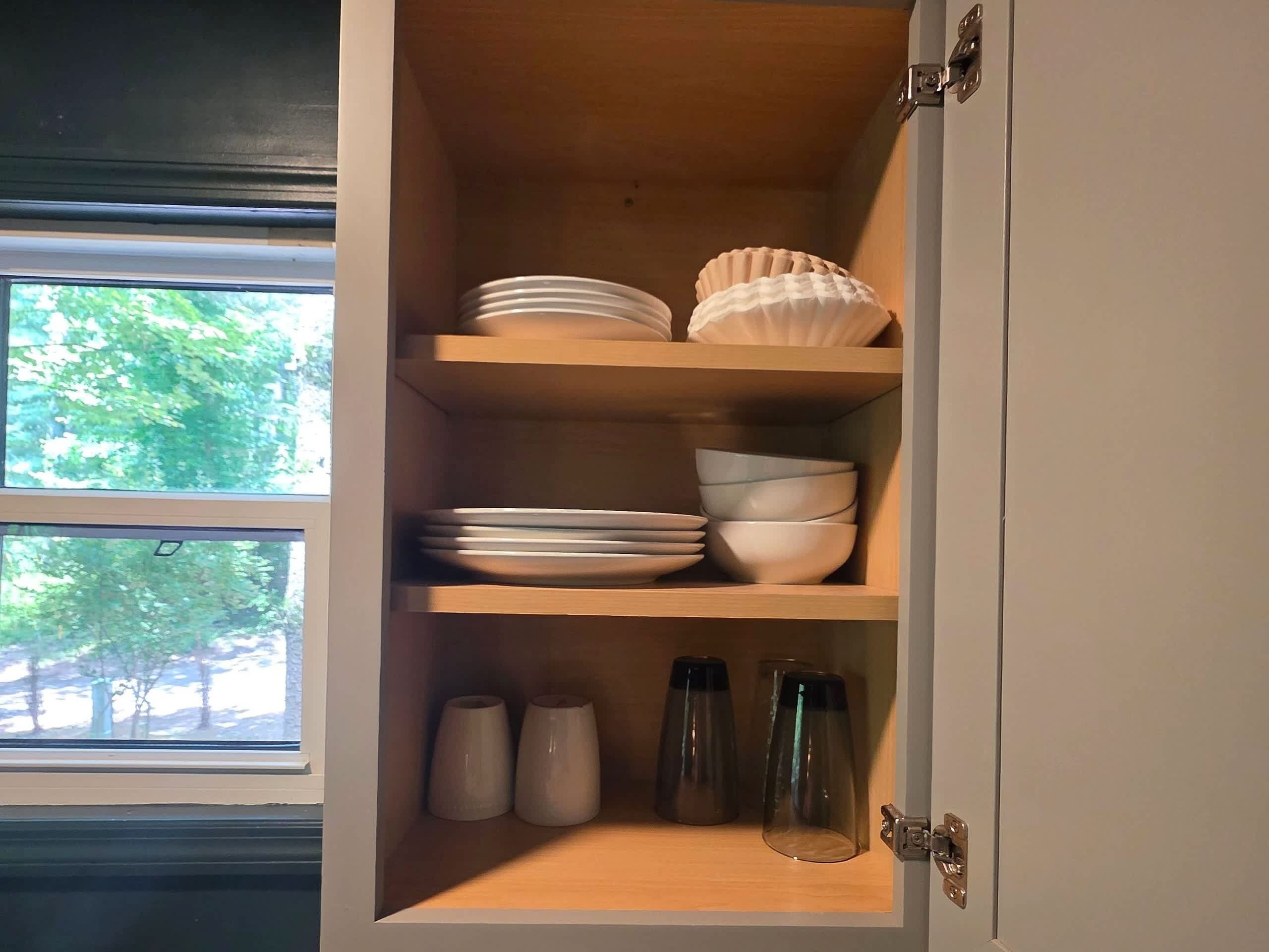 A kitchen cabinet with shelves holding plates, bowls, and glassware.