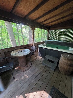A covered outdoor area with a hot tub, a round wooden table, and chairs. - The Old Moonshiners at Avenwood Cabins (new straitsville)