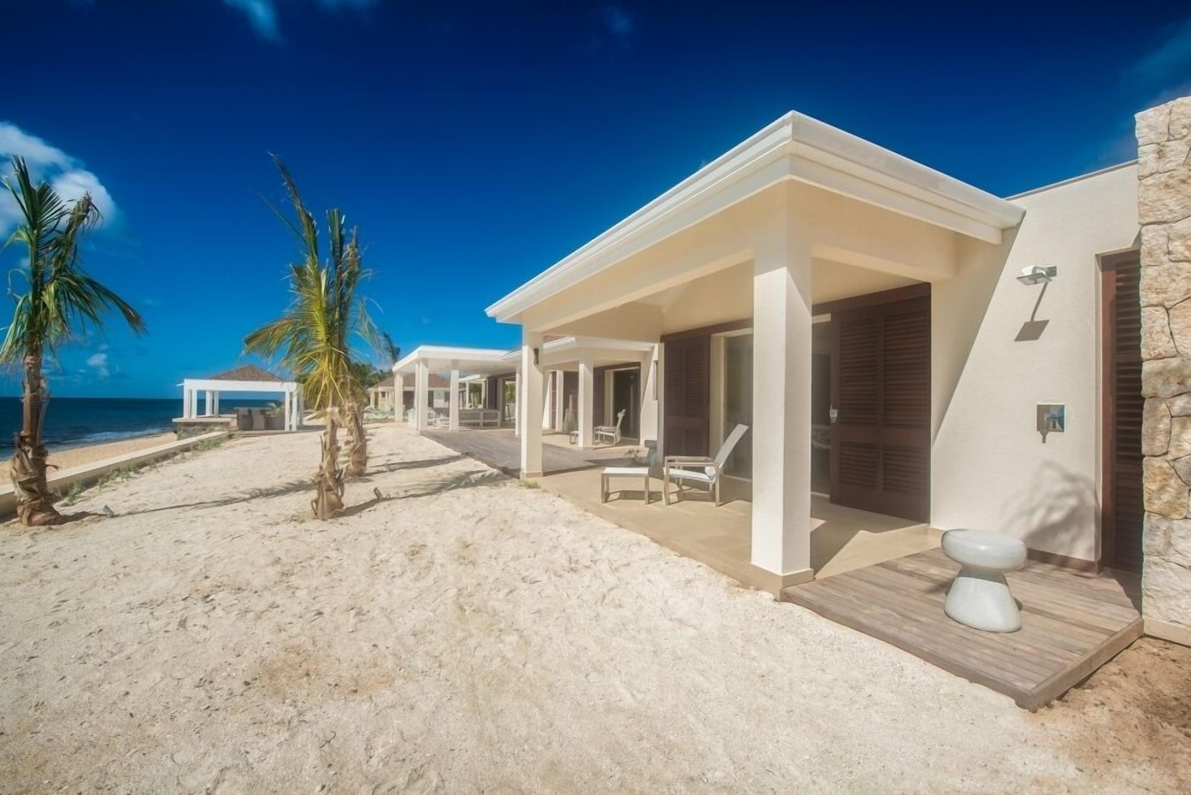 Een strandhuis met een overdekt terras, ligbedden en uitzicht op de oceaan.