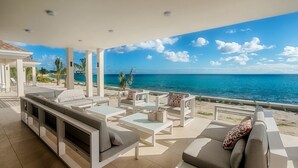 A modern outdoor lounge area with a view of the ocean, featuring a sofa set, coffee table, and a TV. - Villa Turtle Nest  | Beach Front - Located in  Magnificent Baie Longue with Private Pool (Les Terres Basses)