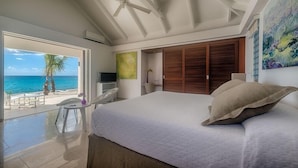 A bedroom with a large bed, a view of the ocean, a ceiling fan, and a wooden wardrobe. - Villa Turtle Nest  | Beach Front - Located in  Magnificent Baie Longue with Private Pool (Les Terres Basses)