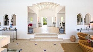 A spacious interior with a high ceiling, a central staircase leading to an outdoor area, and a seating area with wicker furniture. - Villa Oceane  | Ocean View - Located in  Fabulous Terres Basses with Private Pool (Les Terres Basses)