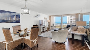 A spacious living area with a glass dining table, wicker chairs, a sofa, and a view of the ocean. - 🌴Gulf Front~ Free Seasonal Beach Chairs -2BR Shoreline Towers 1035 (Destin)