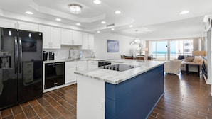A modern kitchen with white cabinets, a black refrigerator, and a blue island. - 🌴Gulf Front~ Free Seasonal Beach Chairs -2BR Shoreline Towers 1035 (Destin)