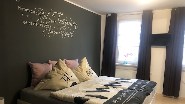 A bedroom with a bed, pillows, a bedside table, and a wall with text.