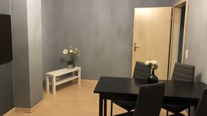 A dining area with a dark wooden table and four chairs, a small white bench, and a vase with flowers on a stand.