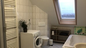 A small, modern bathroom with a washing machine, toilet, and bathtub.