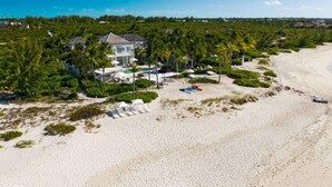 Una proprietà fronte spiaggia con una grande casa, palme e una spiaggia sabbiosa.
