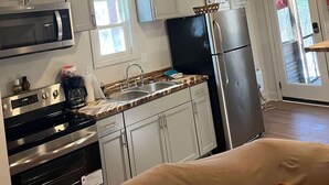 A kitchen with stainless steel appliances, white cabinets, a ceiling fan, and a window.