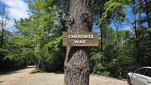 A sign reading 'Cherokee Way' on a tree, a gravel path, and a parked car.