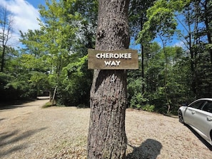 Señal que dice 'Cherokee Way', un árbol, un sendero de grava y un coche aparcado.