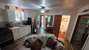 A compact living space with a kitchenette, a sofa with patterned cushions, and a ceiling fan.